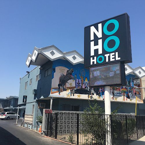 The image shows a street view of the NoHo Hotel, featuring a sign and a blue building with a mural of a bull.