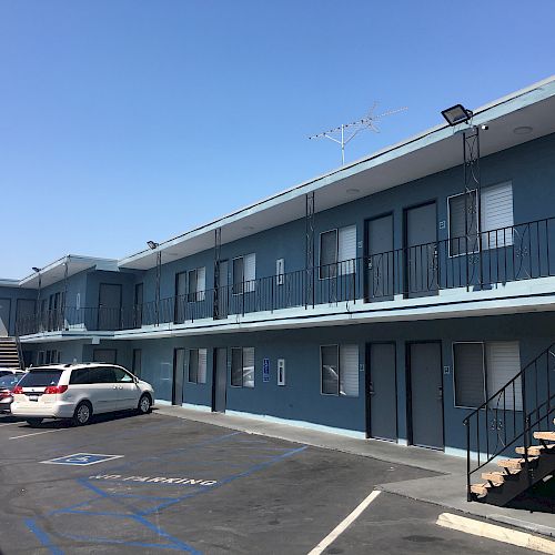 The image shows a two-story motel or apartment building with a parking lot, some parked cars, and outdoor staircases leading to the upper floor.