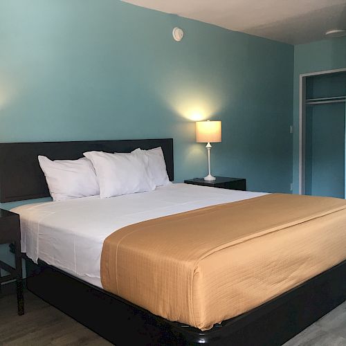 This image shows a bedroom with a neatly made bed, two nightstands with lamps, and an open closet. The walls are painted light blue.