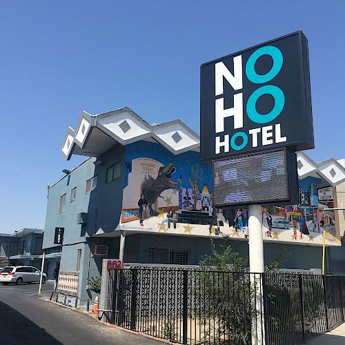 Image of the NoHo Hotel with a large sign displaying the hotel's name, situated in a blue building with unique architecture and mural art.